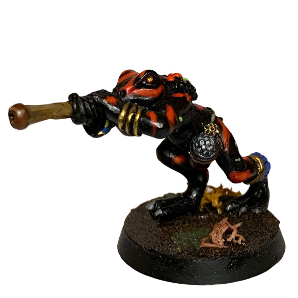 A resin miniature figure of a Bizaza tribal warrior with a blowpipe, dressed in a loincloth and bracelets, carrying a dart pouch. The figure is black, red, and gray, and is shown on a 20mm round base.