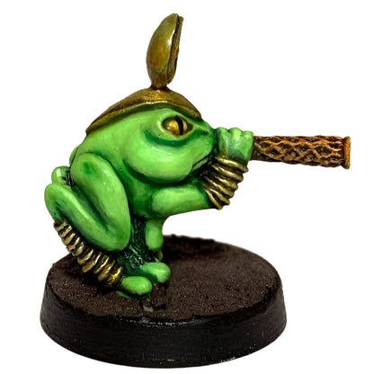 A miniature figure of a green frog with a golden blowpipe, designed for tabletop gaming.
