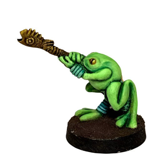 A miniature figurine of a green frog with a blowpipe, designed for tabletop gaming.